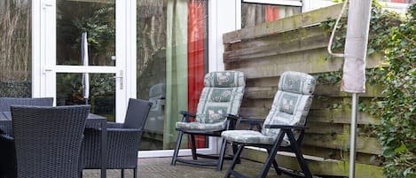Un patio con mobiliario de mimbre y sillas estampadas, una valla de madera y una puerta de cristal con el número 90 a la vista.
