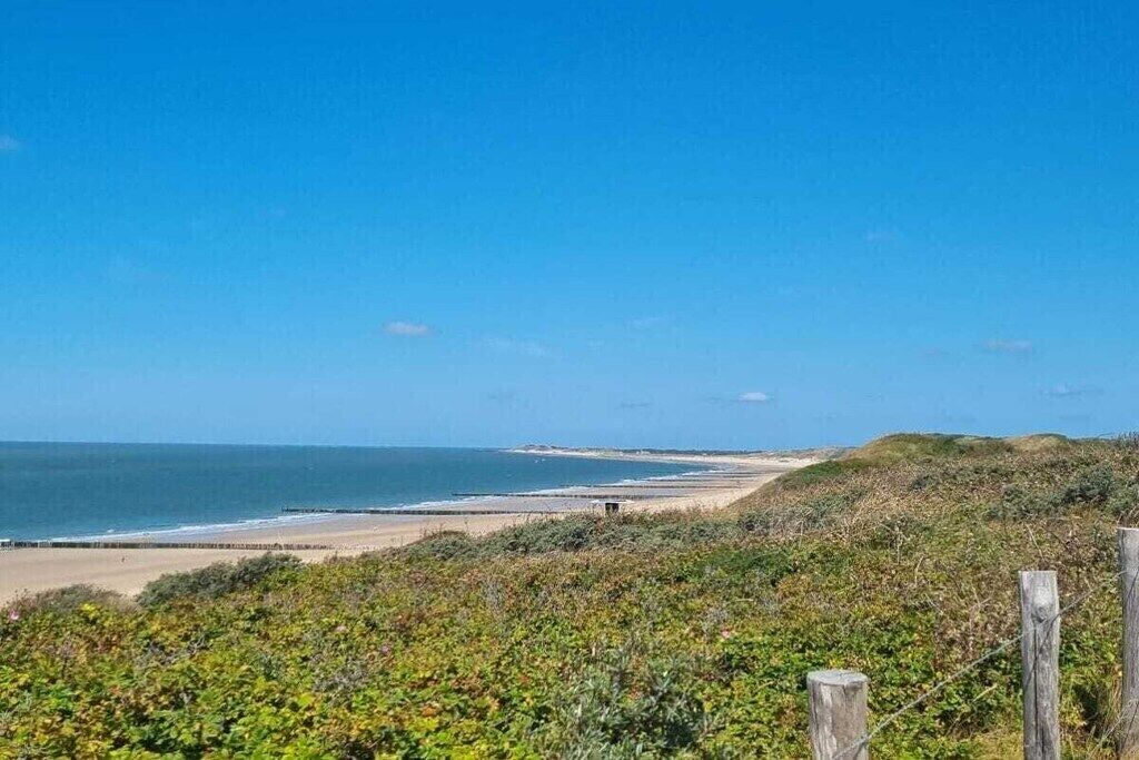 Un paysage côtier avec une plage de sable, une clôture en bois et une végétation luxuriante.