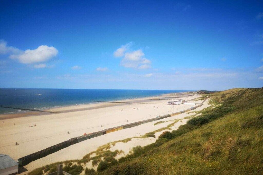 Un paysage côtier avec une plage de sable, une colline herbeuse et un ciel bleu dégagé.