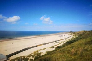 Un paysage côtier avec une plage de sable, une colline herbeuse et un ciel bleu dégagé.