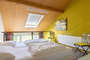 Une chambre avec deux lits, un puits de lumière, un radiateur et un mur jaune.