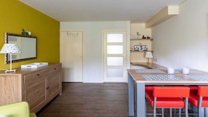 A compact room with a wooden dresser, a desk with chairs, a mirror, and a door leading to another room. - De Woeste Hoeve No. 90 (Zoutelande)
