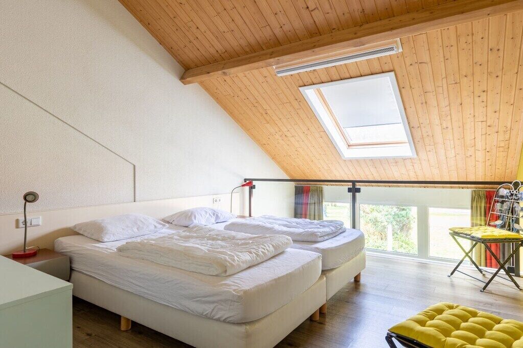 Une chambre avec deux lits, une lucarne, un bureau et un pouf jaune.