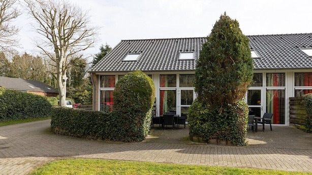 A two-story building with a tiled roof, a paved courtyard, and a well-maintained lawn. - De Woeste Hoeve No. 90 (Zoutelande)