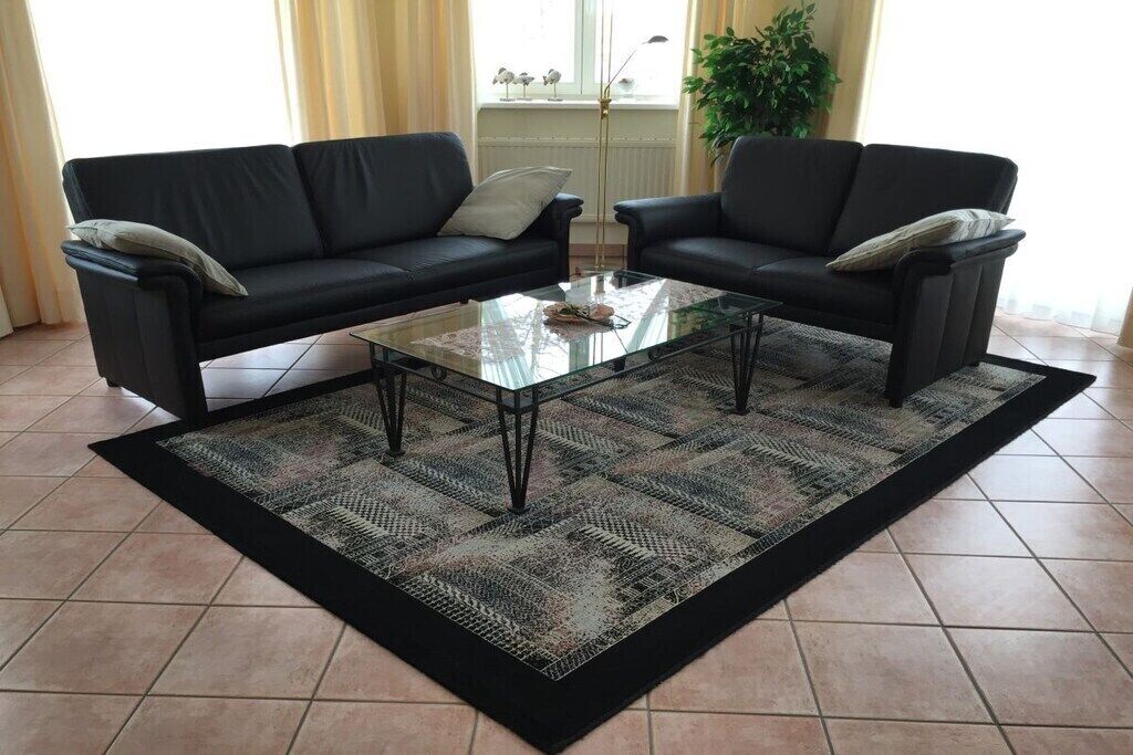 Un salon avec deux canapés noirs, une table basse en verre et un tapis à motifs.
