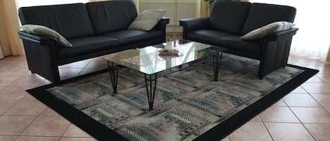 A living room with two black sofas, a glass coffee table, and a patterned rug.