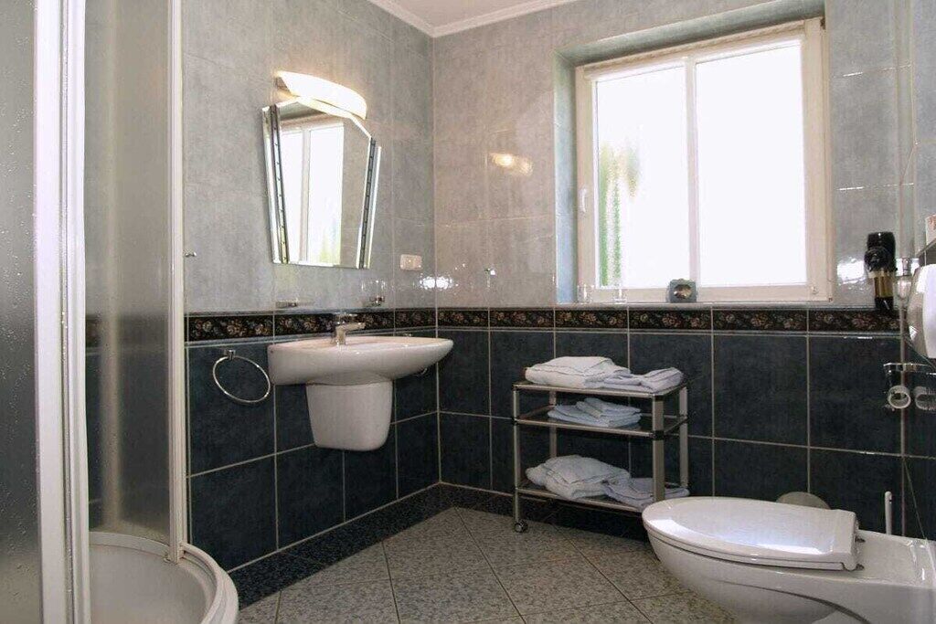 A bathroom with a sink, mirror, toilet, and a window.
