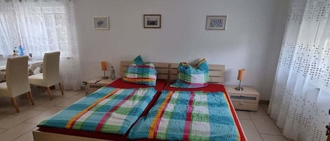 Un dormitorio con una cama, dos mesitas de noche, una silla y cortinas.