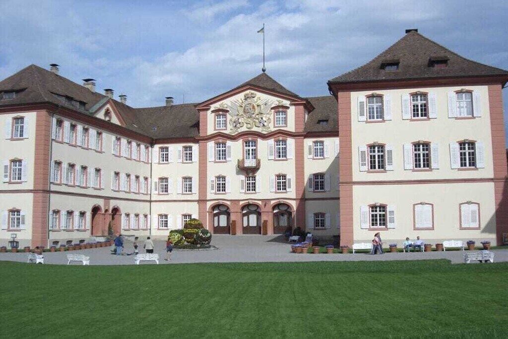 A large, symmetrical building with a central entrance, multiple windows, and a flag.