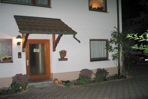 Un edificio con toldo de tejas, una puerta con un letrero y una ventana con cortina.