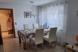 Zona pranzo con tavolo apparecchiato per quattro, sedie, lampadario e finestra con tende a motivi.