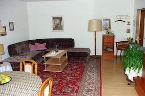 En stue med sofa, sofabord, spisebord med frugt, et mønstret tæppe og en lampe.