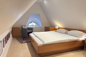 Ein Schlafzimmer mit schrägem Dach, einem Bett, einem Schreibtisch und einem Fenster.