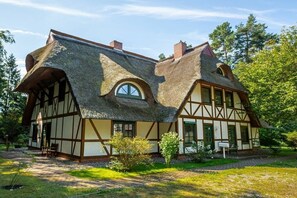 A traditional half-timbered house with a steeply pitched thatched roof, a visible chimney, and a small garden area with a bench. - Holiday apartment with 1 bedroom (Born am Darß)