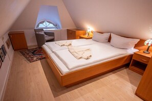A bedroom with a wooden bed, a desk, a chair, a small table with a lamp, and a window with a view. - Holiday apartment with 1 bedroom (Born am Darß)