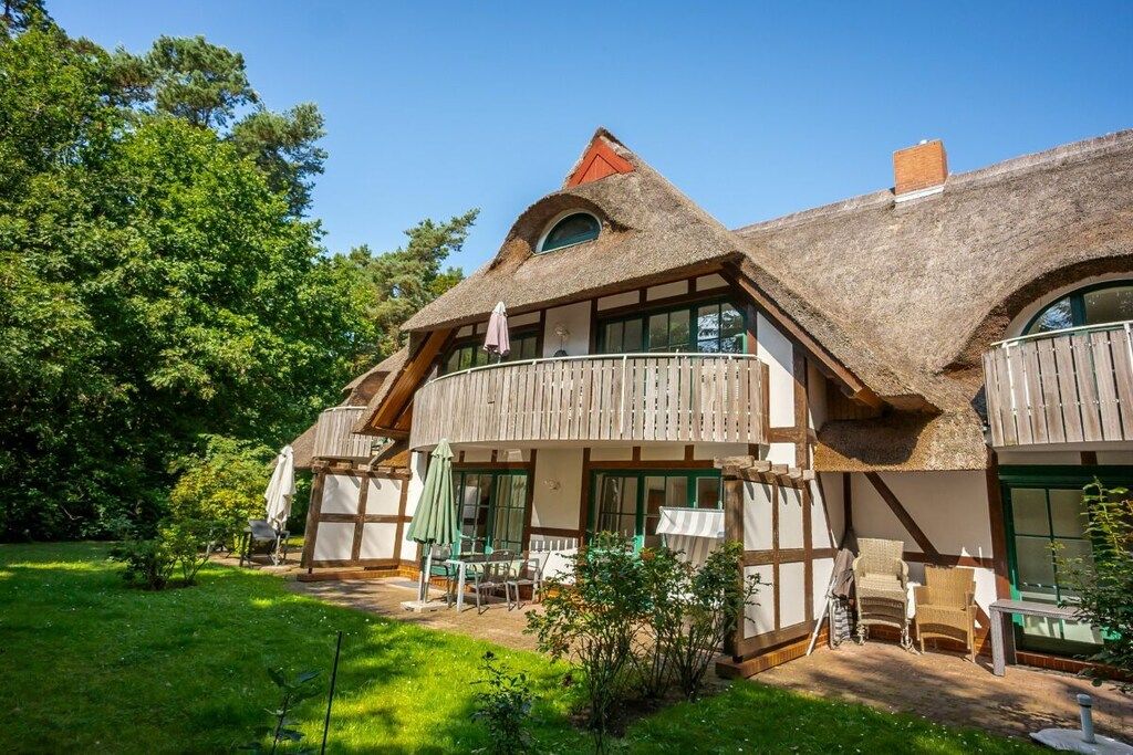Une maison traditionnelle avec un toit de chaume, des balcons en bois et un jardin aménagé avec du mobilier d’extérieur.