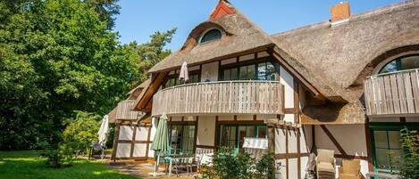 A traditional house with a thatched roof, wooden balconies, and a garden area with outdoor furniture.