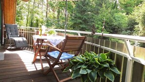 Une terrasse en bois, agrémentée d’une table et de chaises, entourée d’une rambarde et offrant une vue sur une zone boisée.