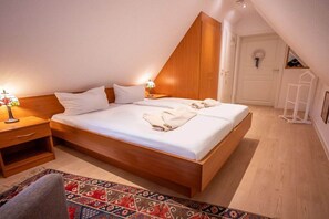 Een hotelkamer met een houten bed, nachtkastjes, een kamerkleed met een patroon en een witte deur met een krans.