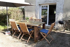 Ein Essbereich im Freien mit Holztisch und -stühlen, einem Grill und einem großen Sonnenschirm.