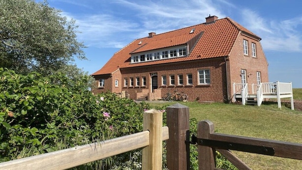 A two-story brick house with a red-tiled roof, a front porch with white railings, and a bicycle parked outside. - Holiday apartment in Juist with swimming pool (Juist)