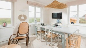 A bright kitchen with a large window, a dining table with chairs, and a hanging light fixture. - Holiday apartment in Juist with swimming pool (Juist)