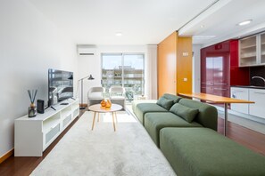 A modern living room with a sofa, a TV, and a small table. There is a balcony with a view of buildings. - Spacious apartment with balcony • Porto • 2 bedrooms (Porto)