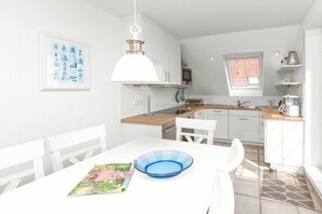 Eine moderne Küche mit weißen Schränken, einer Holzausziehtafel, einem Esstisch mit Stühlen und einer blauen Schüssel auf dem Tisch.