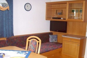 A small living area with a sofa, a television, a cabinet with glassware, and a clock on the wall. - Holiday apartment with 2 bedrooms (Schwendau\/Mayrhofen)