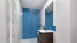Un baño moderno con cabina de ducha de vidrio, azulejos blancos y azules, un lavabo blanco y un espejo.