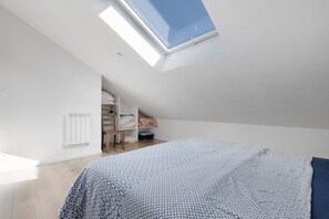 A bedroom with a skylight, a bed with patterned bedding, a radiator, and a built-in shelving unit.