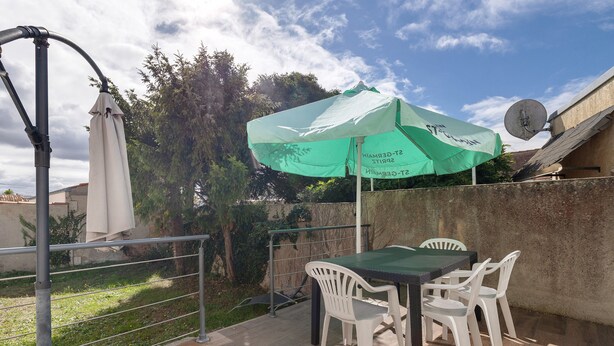 Un patio al aire libre con una mesa y sillas, un parasol verde y una antena parabólica.