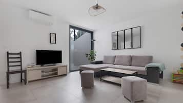 A modern living room with a flat-screen TV, a sofa, a coffee table, and a dining table.