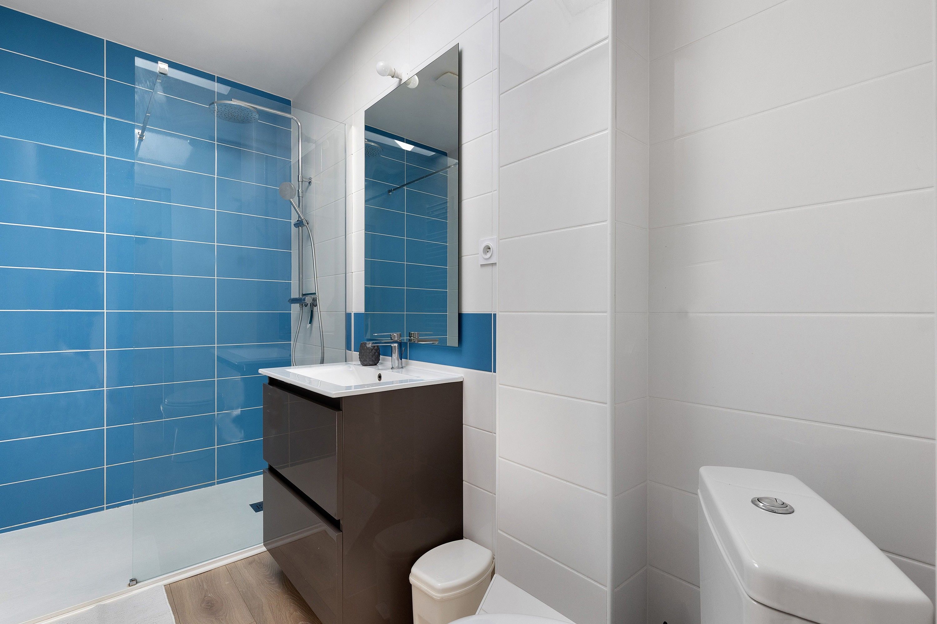 Une salle de bain moderne avec des carreaux bleus, un lavabo blanc et des toilettes.