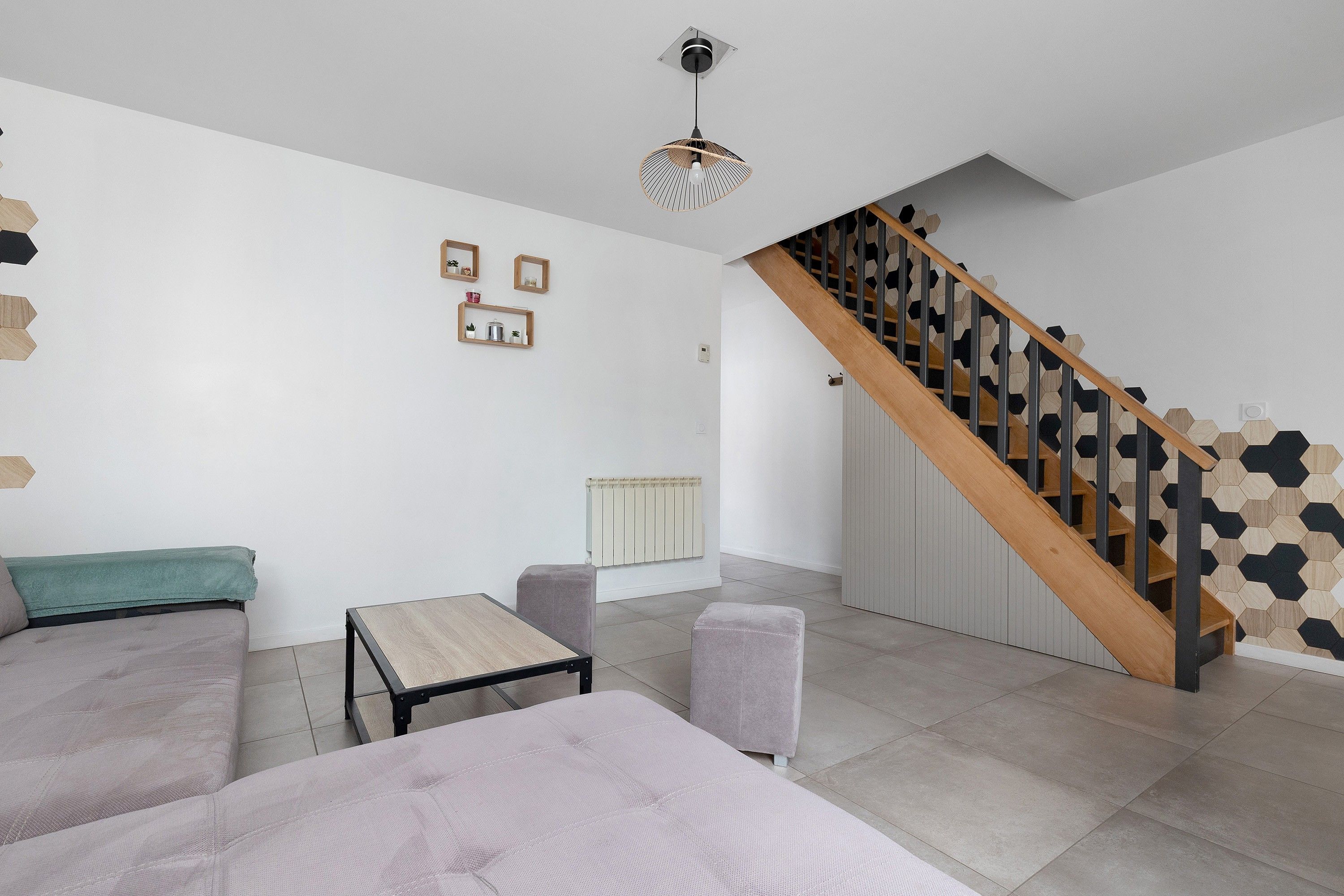 A modern living room with a sofa, a small table, a staircase with a wooden handrail, and a wall with hexagonal patterns.