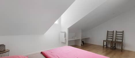 A bedroom with a sloped ceiling, a bed with pink bedding, two wooden chairs, and a radiator.