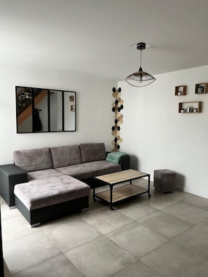 Ein modernes Wohnzimmer mit einer Eckcouch, einem Couchtisch, einer Pendelleuchte und einem Wandspiegel.