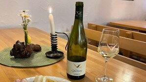 Een eettafel met een wijnfles, een glas, een kaars, een vaas met bloemen en borden met eten.