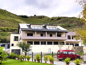 Um edifício moderno de dois andares com telhado plano e várias janelas, com um veículo vermelho estacionado na frente.