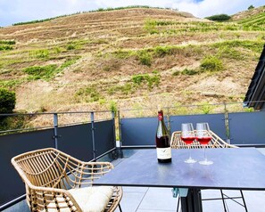 Um terraço com mesa, cadeira de vime e uma garrafa de vinho com copos.