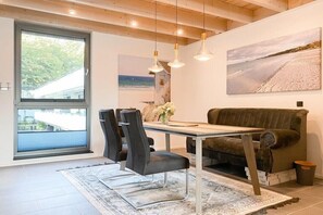 Ein moderner Wohnraum mit Essbereich, einer Couch und einem großen Fenster mit Blick ins Freie.