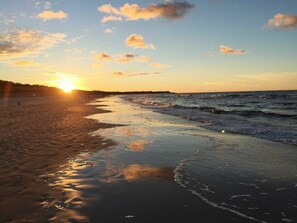 A beach with the sun setting over the horizon, waves gently lapping at the shore, and a clear sky with scattered clouds. - in the Lake Park "heringsdorf" (Heringsdorf)