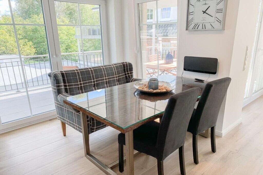 A dining area with a glass table, two chairs, a plaid sofa, and a clock on the wall.