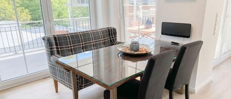 Un comedor con una mesa de vidrio, dos sillas, un sofá a cuadros y un reloj en la pared.