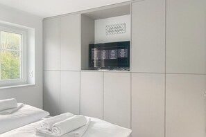 Ein Schlafzimmer mit Bett, Fenster, Kleiderschrank und Bedienfeld an der Wand.