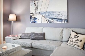A modern living room with a sofa, two pillows, a lamp, and a framed picture of a sailboat on the wall. - Holiday apartment with 1 bedroom (Scharbeutz)