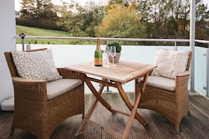 A wooden deck with two wicker chairs and a table, a bottle of champagne, and two glasses. - Holiday apartment with 1 bedroom (Scharbeutz)