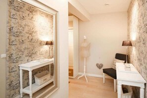 Une pièce comprenant une console blanche, une chaise blanche, un lampadaire et un miroir agrémenté d’un papier peint à motifs.