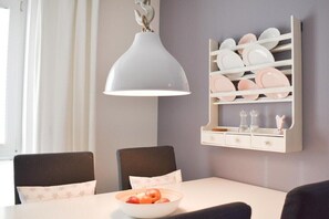 A dining area with a white table, black chairs, a bowl of fruit, a pendant light, and a wall-mounted plate rack. - Holiday apartment with 1 bedroom (Scharbeutz)