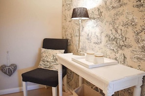 A room with a white table, a black chair, a lamp, and a wall with a floral pattern. - Holiday apartment with 1 bedroom (Scharbeutz)